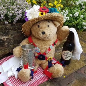 A teddy bear in morris dancing kit, holding a tankard of ale